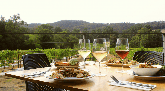 Side view of a Steel's Gate lunch table setting with savoury dishes and wine - set against a backdrop of vineyards and tree covered hills
